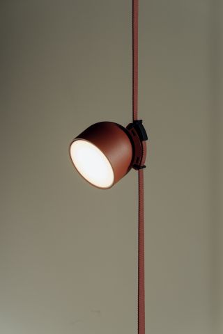A red lamp shaped as a semi-sphere, hanging from a thick red textile band
