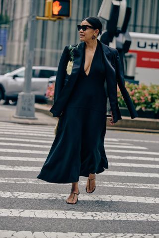 Sherri McMullen crossing the street in a black dress, black blazer with a floral decal, and strappy heeled sandals.