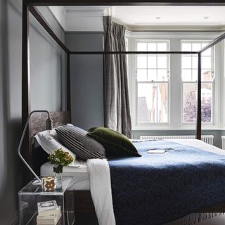 Bedroom decorated in muted colours with a four poster bed and night table and grey curtains. A renovated Victorian house in London, home for Sue and Matt.
