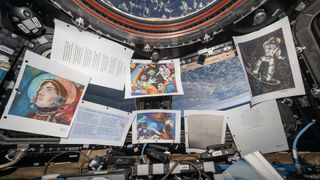 printed copies of paintings, drawings and poetry are hung on window panes aboard a space station