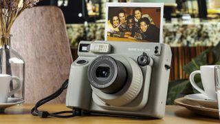 Fujifilm Instax Wide 400 camera in sage green, on a wooden table with instant print of a group selfie
