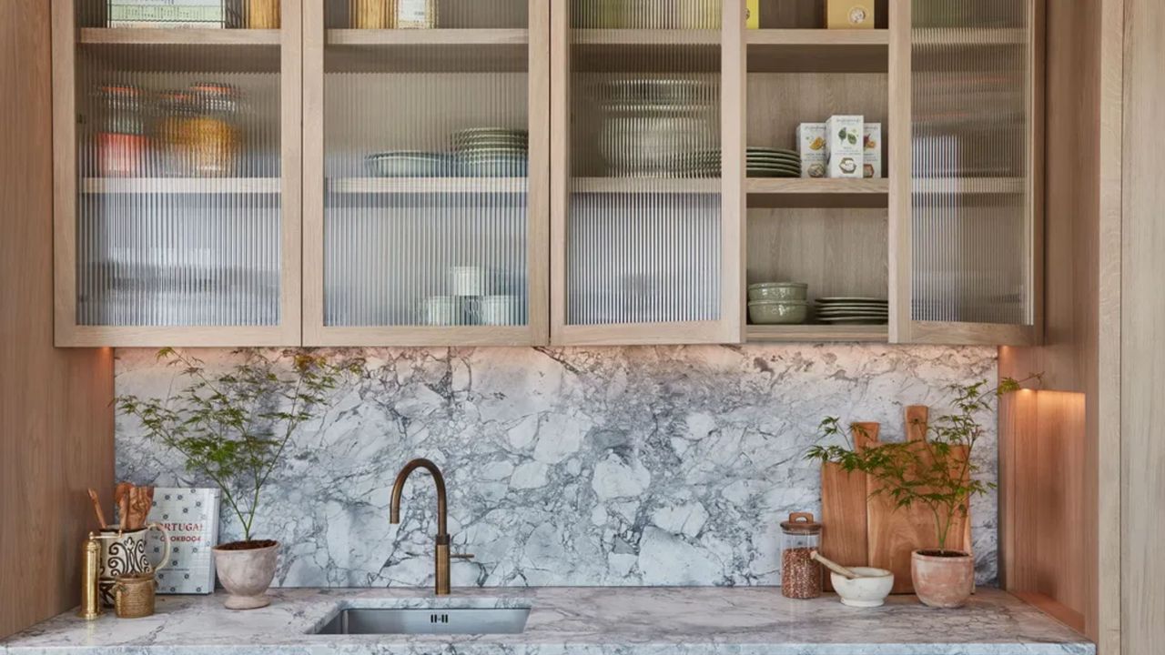 a close up of a wood and marble kitchen with reeded glass cabinet uppers