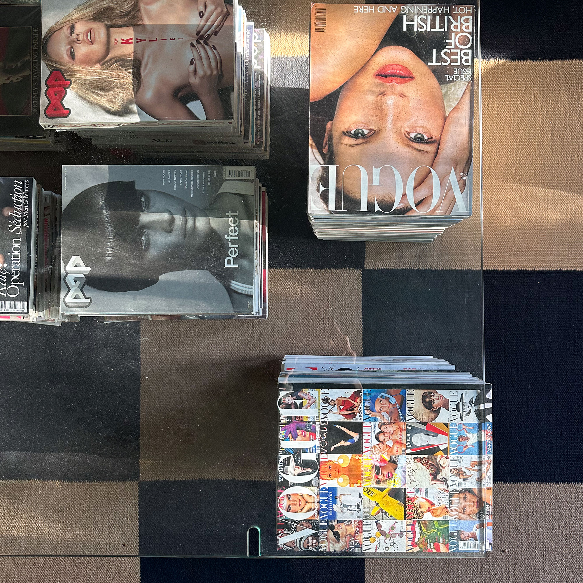 Glass topped coffee table propped up with marble and stacks of magazines including Vogue and Pop