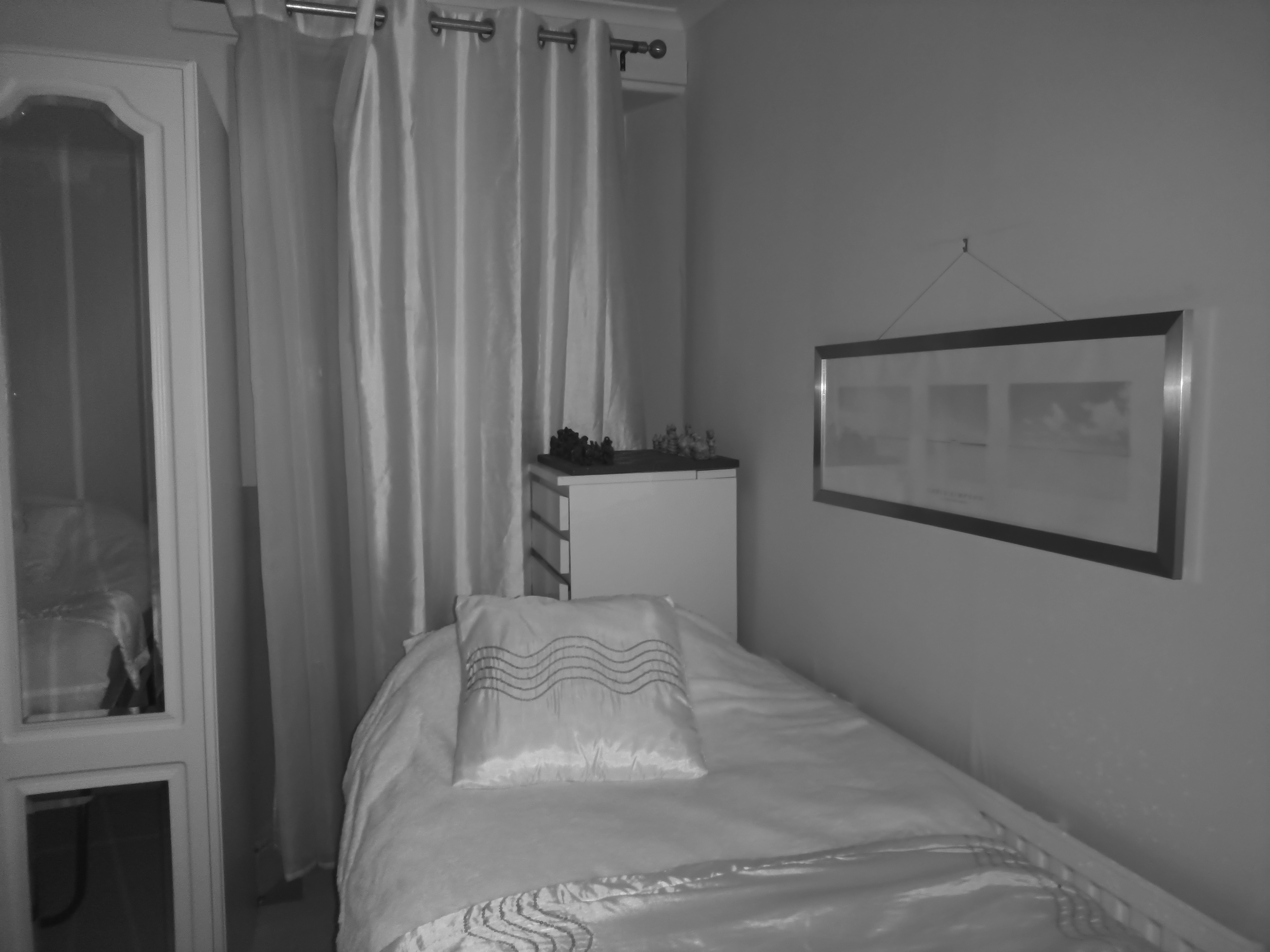 A black-and-white photo of a bedroom with a bed and a large white wardrobe featuring mirrored doors is shown.