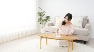 An Asian woman cleaning a coffee table in a brightly lit room