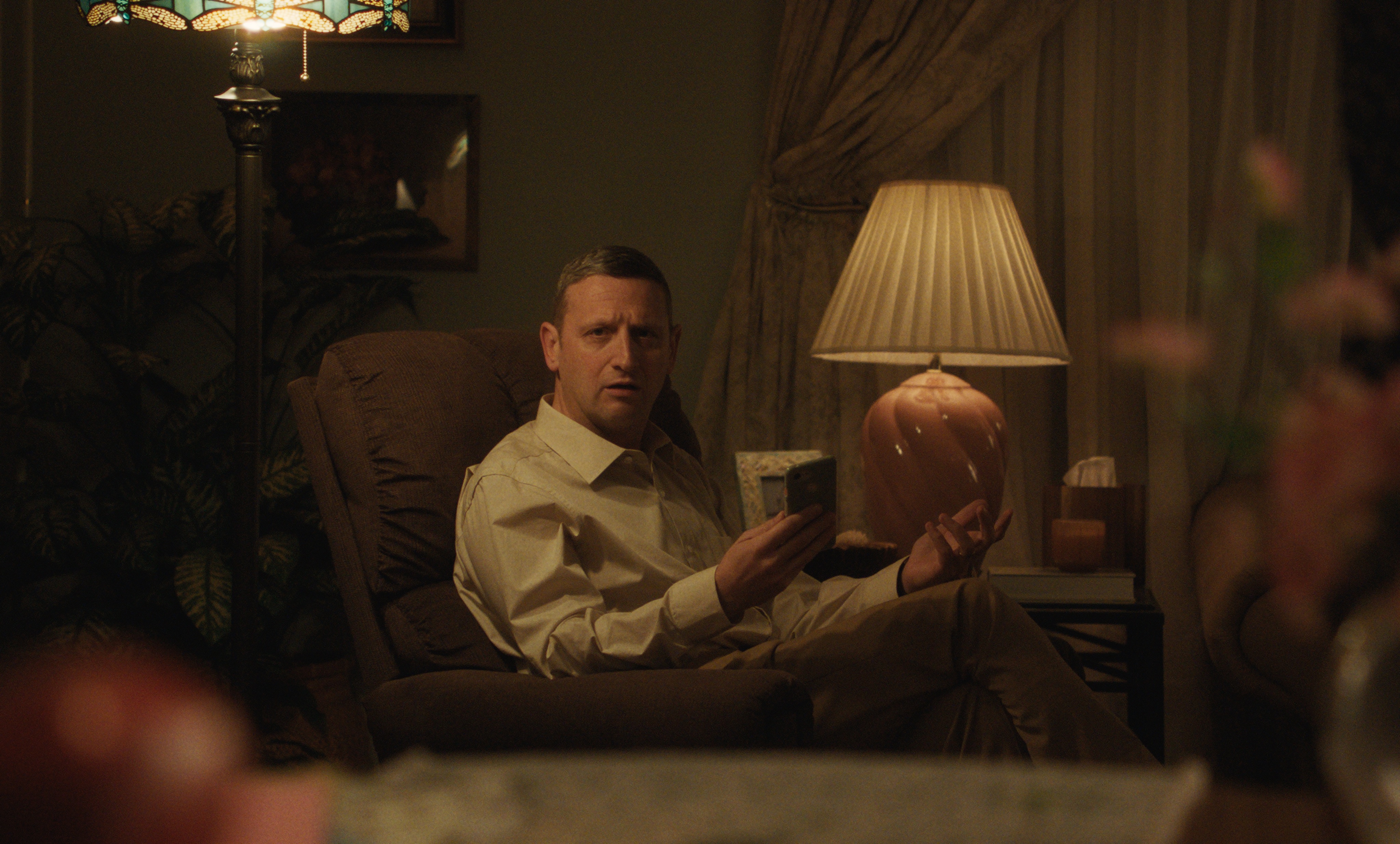 tim robinson as craig looking surprised sitting in a living room chair in the movie friendship