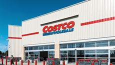 A customer walks out of a Costco Wholesale store on a bright, sunny day.