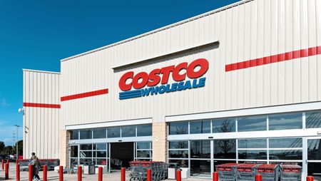 A customer walks out of a Costco Wholesale store on a bright, sunny day.
