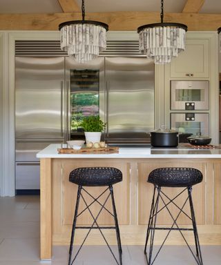 A light wood kitchen with a small peninsula with black barstools and white marble countertops
