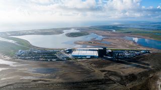 a collection of buildings and parked cars sits near an estuary and the ocean, seen from the air