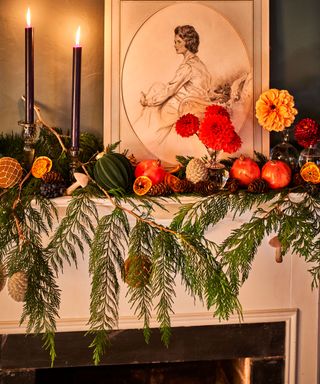 Mantelpiece with framed picture and lit candles, decorated with flowers, foliage and dried fruits