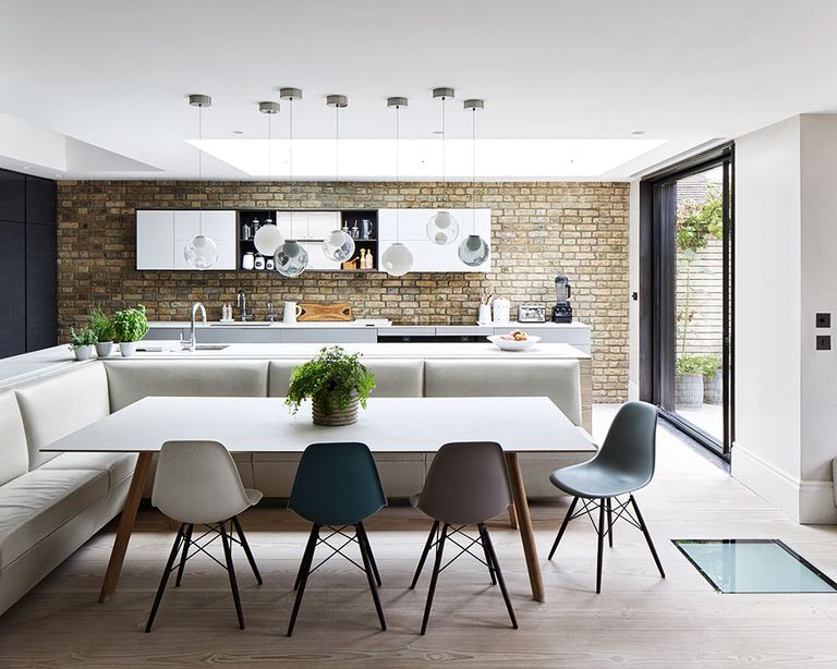 An example of how to plan a kitchen extension showing a large kitchen with pendant lighting over an island behind an L-shaped dining area with banquette seating