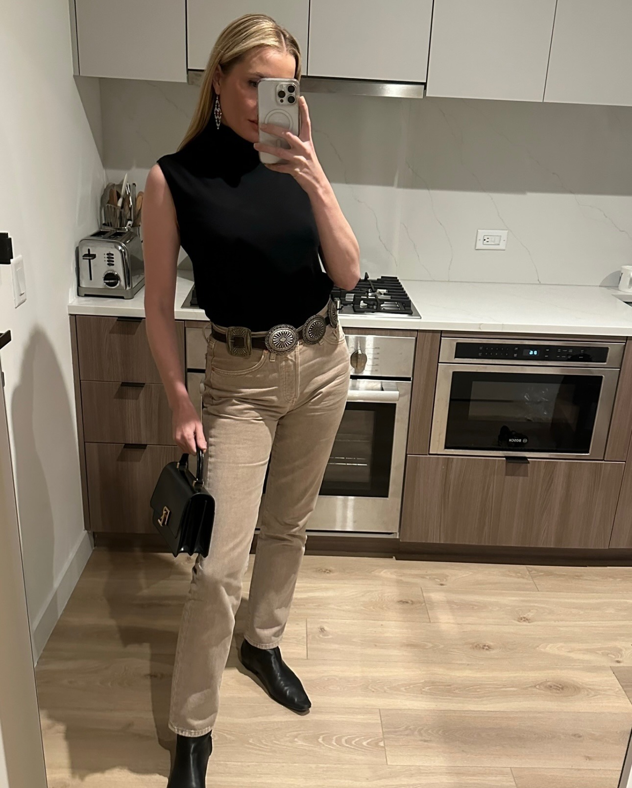 Kristen Nichols wearing a sleeveless turtleneck, khaki high-waisted jeans, and Western ankle boots.