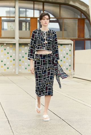 Model inblack Chanel skirt suit with colourful geometric motif walks in runway show on concrete rooftop