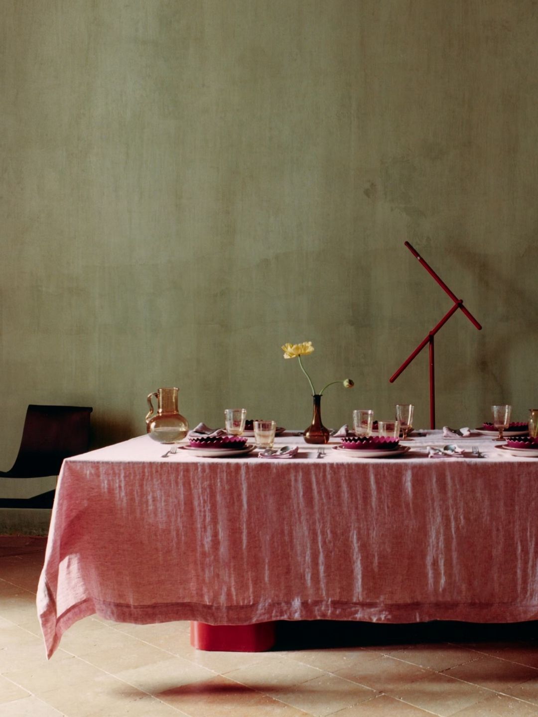 A pastel pink table set iwth pink tableware and glassware in an olive green room.