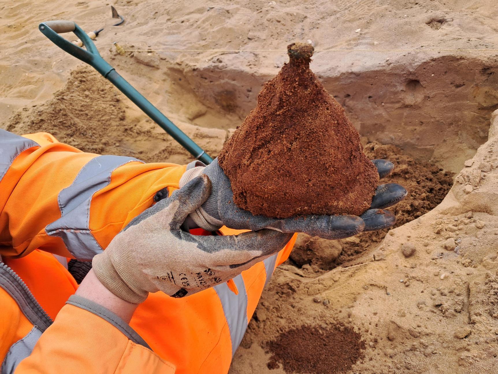 An anglo saxon shield boss being held at an excavation site by a gloved researcher