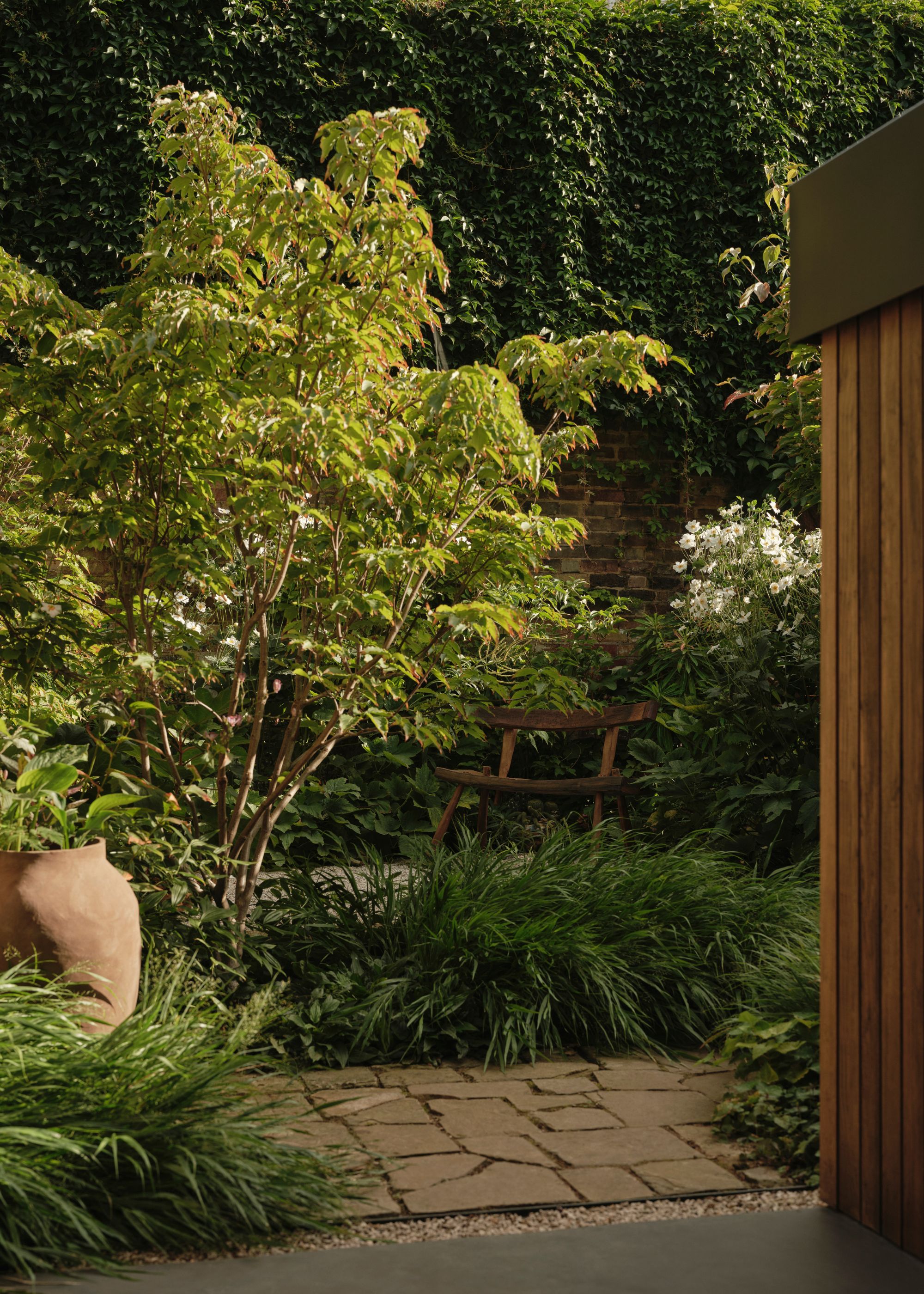 A garden drenched backyard with a terracotta planter, stone pathways, and a wooden bench