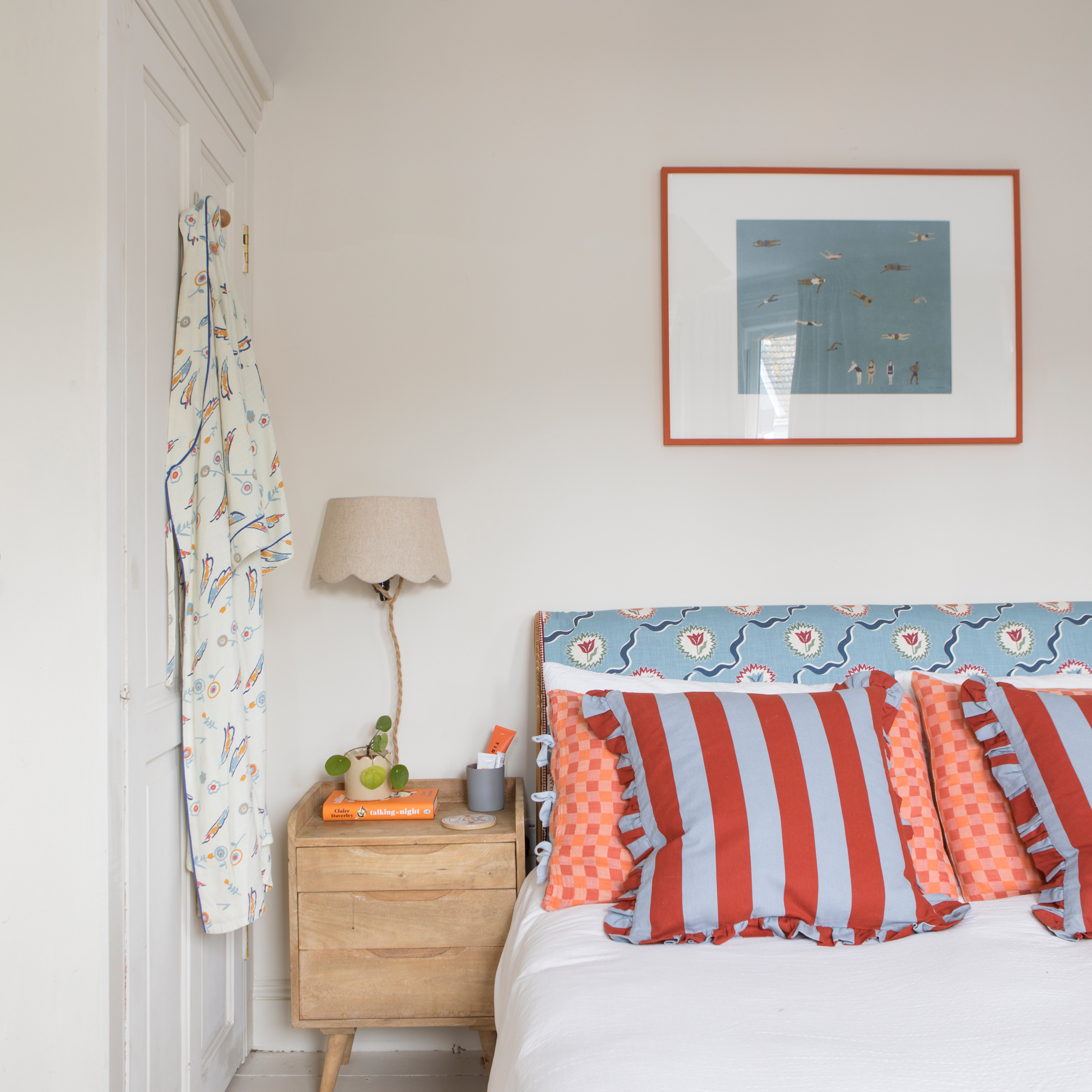 a bedroom with a patterned fabric covered headboard, wooden bedside table and white fitted wardrobe