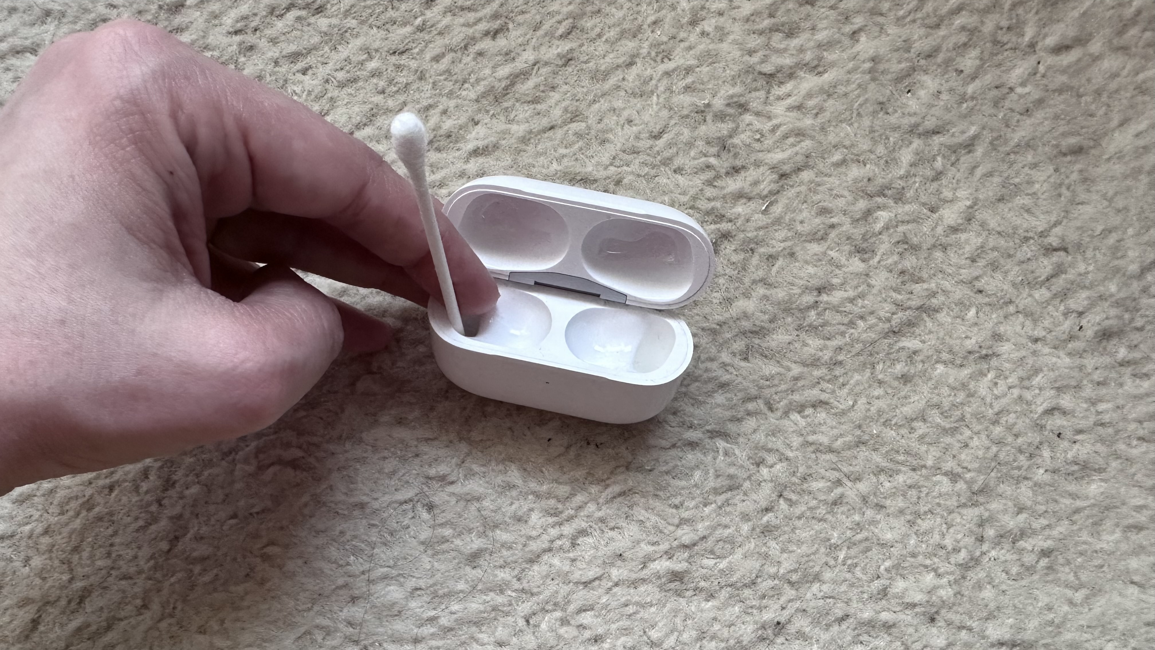 An Apple AirPods case with a cotton bud sticking out of it.