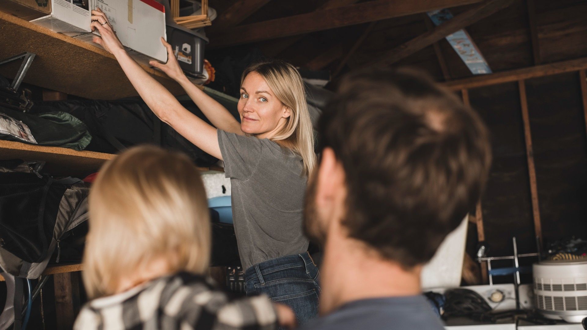 woman reaching for a box in a garage, with her family looking on