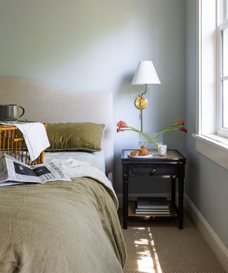 blue painted bedroom with green bed linens and flowers in a vase on the nightstand