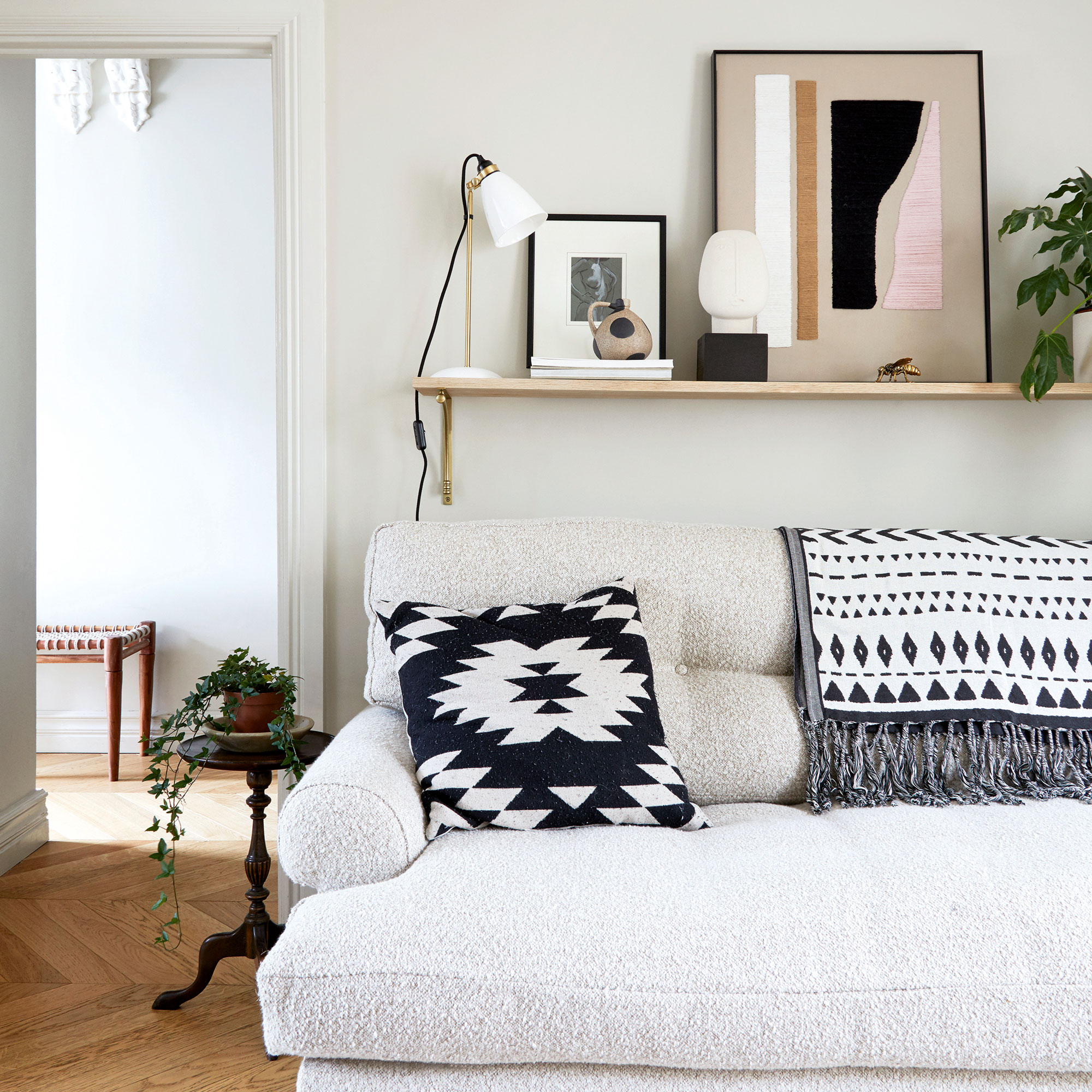 Grey living room with a boucle sofa, small black side table, and shelf over the sofa