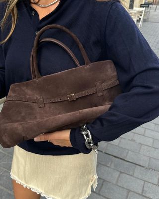 Woman holding a brown suede handbag.