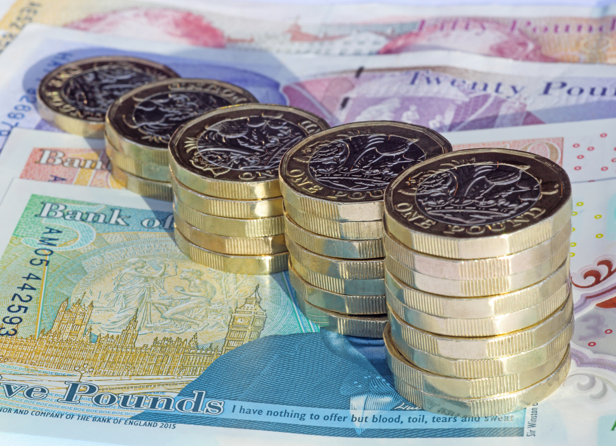 Pound coins in growing piles on top of UK bank notes