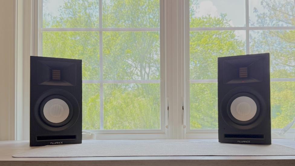 Fluance Ri71 bookshelf powered speakers on a windowsill, with trees outside the window.