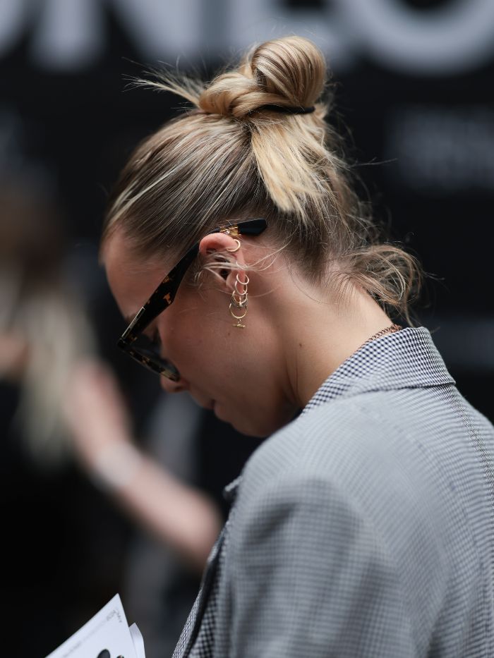 A woman at London Fashion Week wearing a grey blazer and sunglasses with a slicked-back bun