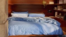 Blue pinstriped Parachute for Target cotton duvet set styled atop of a wood-clad mid-century bedroom accented with books, plants, and sculptural objects