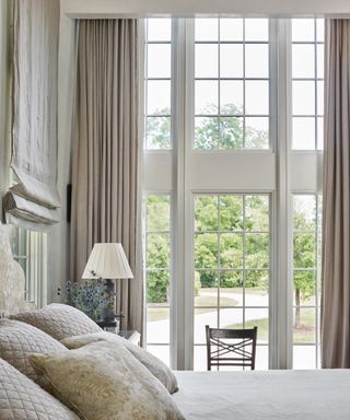 A bedroom with floor-to-ceiling windows, and taupe soft furnishings