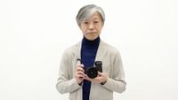 Sigma CEO, Kazuto Yamaki, against a white background holding a Sigma fp L camera