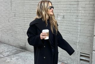 Eliza Huber wearing a black long coat, navy blue sweater, and navy trousers.