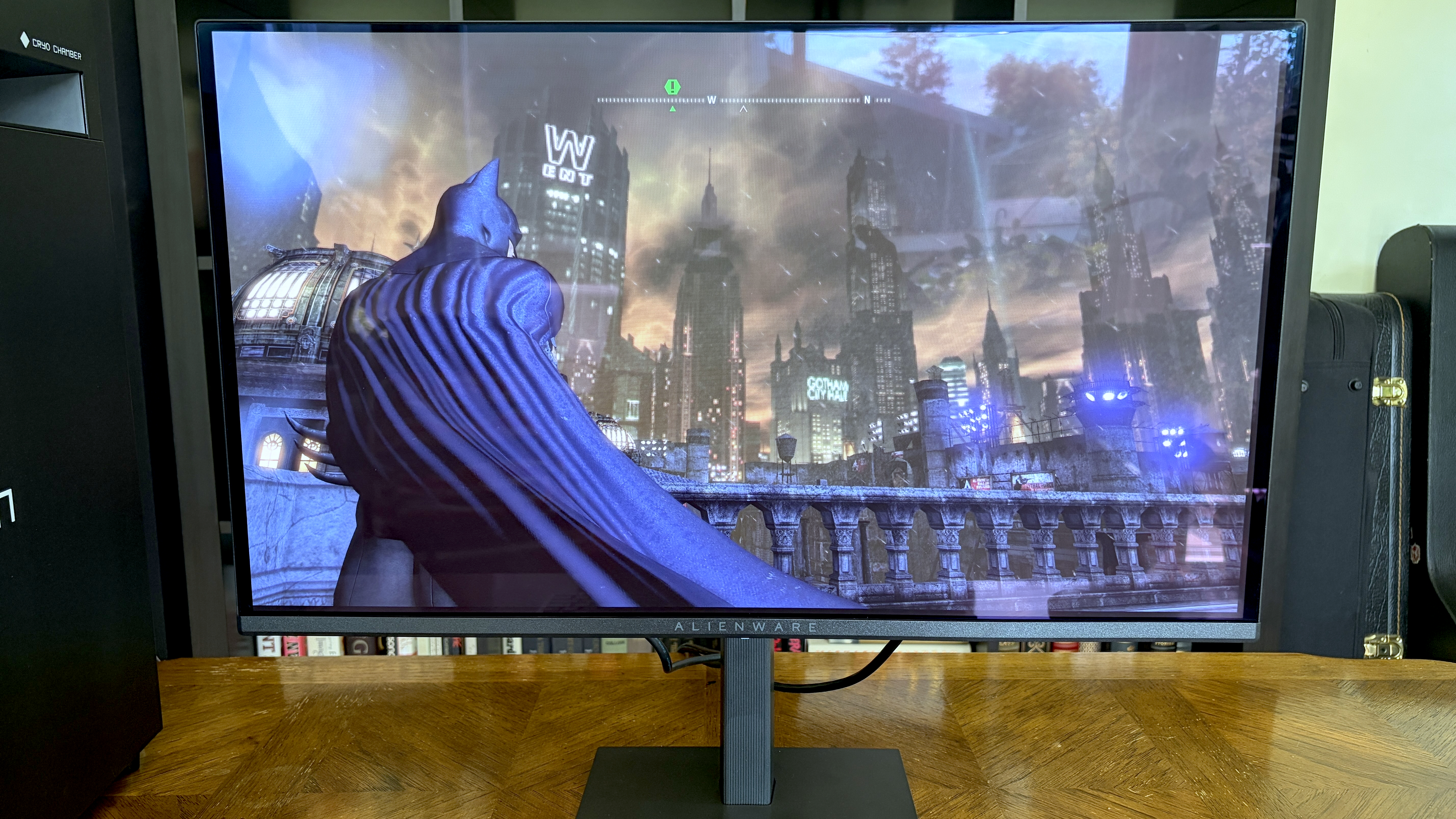 A close-up of a monitor displaying a dark, atmospheric video game scene featuring a superhero character overlooking a cityscape with skyscrapers and a stormy sky.