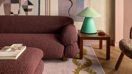 burgundy boucle sofa with pink mural on the wall behind, mint green table lamp, pink and mustard rug, and timber parquetry floors