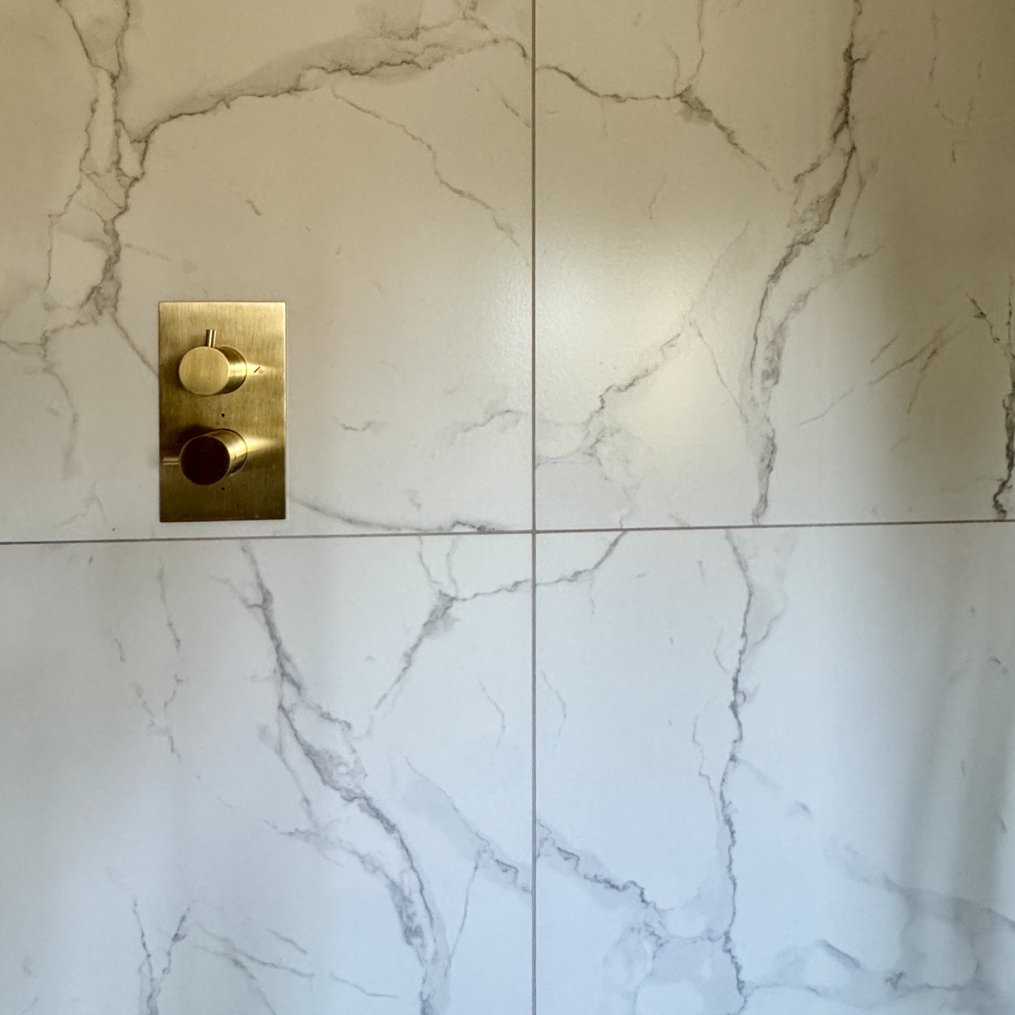 close up of marble look tiles with brass shower controls