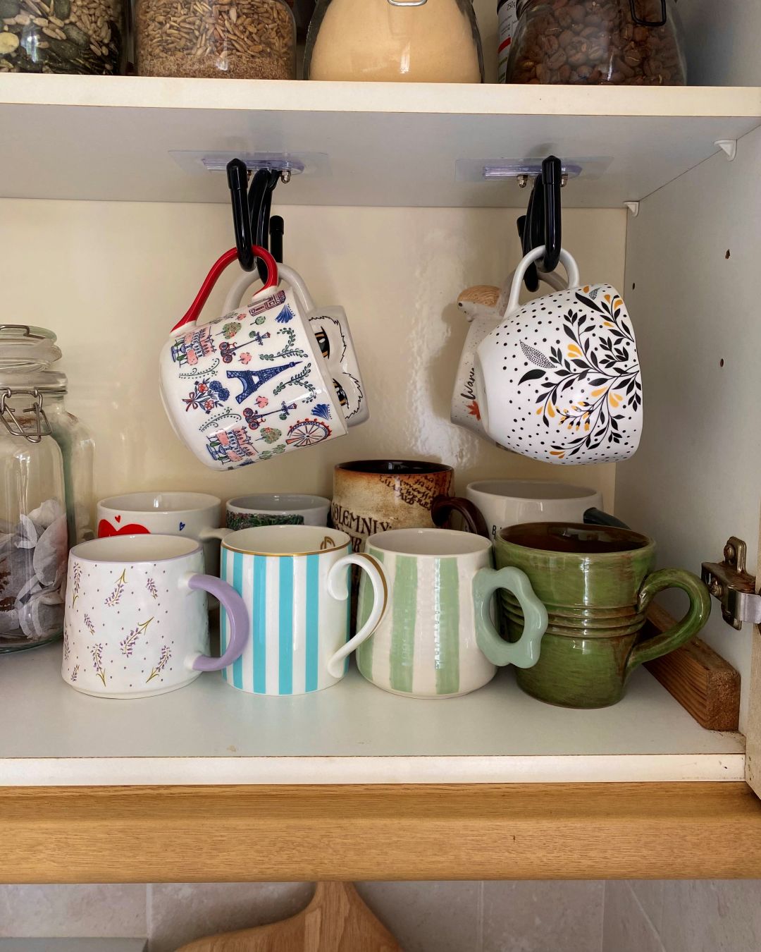 mugs hanging from hooks inside a kitchen cupboard to show small kitchen storage essentials