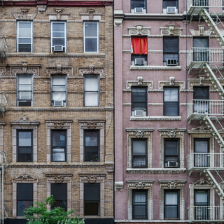 Two older New York City apartment buildings, photographed from the outside, with a fire escape pictured on the right of the image.