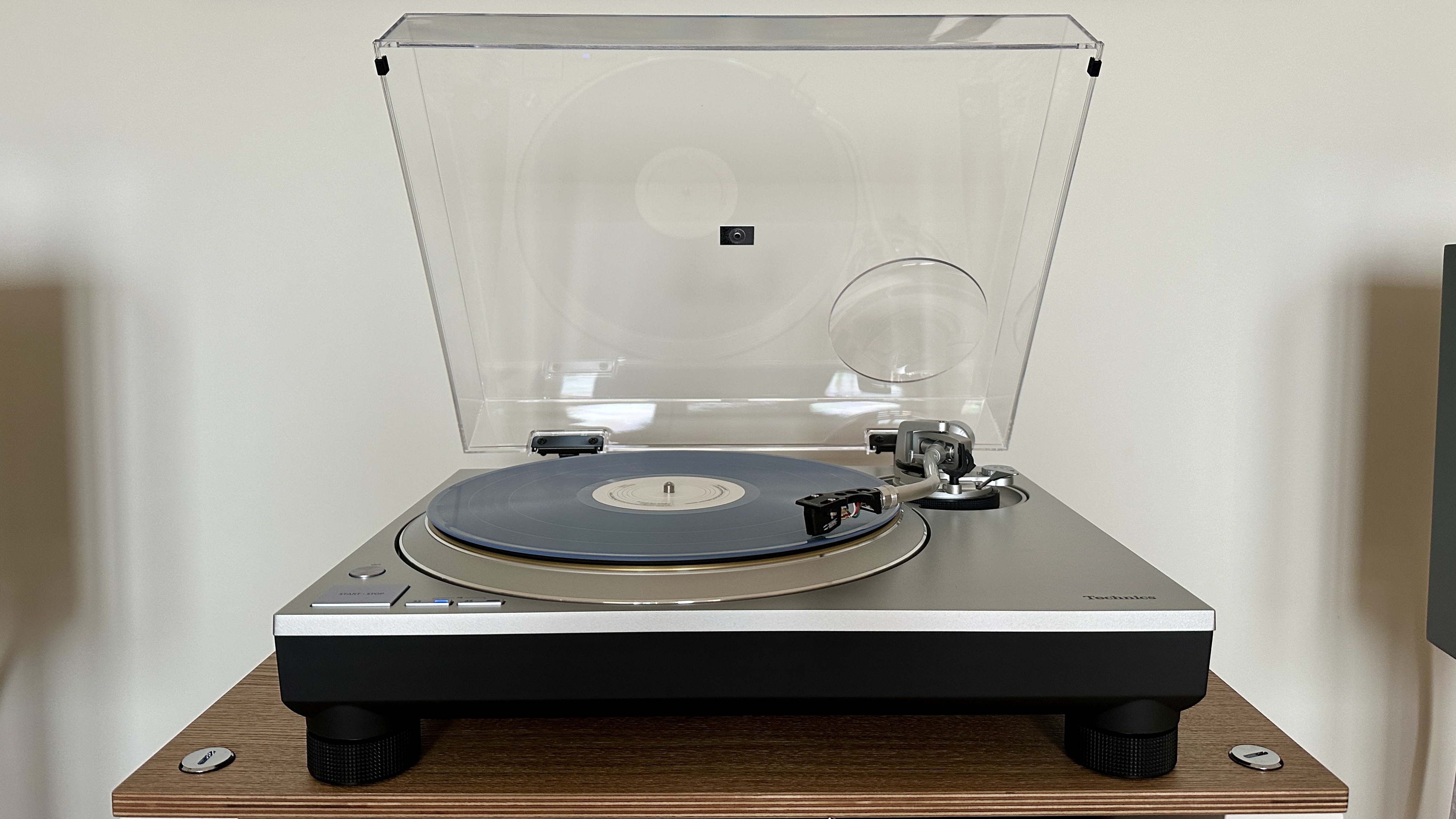 Technics SL-1300G turntable, with the dust cover open, on a wooden platform.