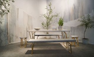 White natural wash walls, grey marble effect floor, white table, two benches, two stools with marble stone tops and gold frames, white stone potted plants and small trees, white bowl on the table top