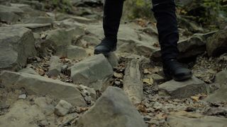 A person wearing black hiking shoes standing on some rocks