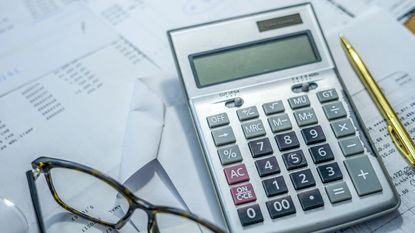 A calculator on top of financial paperwork next to a pair of eyeglasses.