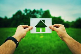 Man holding up picture of house against a backdrop of a field