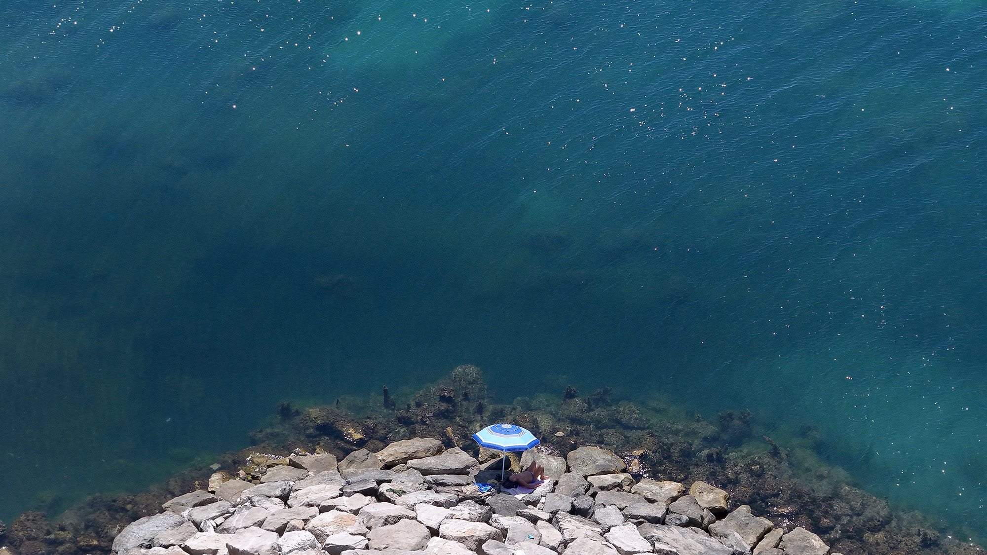 A man sits under an umbrella during a heatwave in front of the sea in Durres, Albania