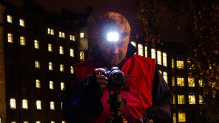 Man in front of large building at night looking at his camera using the best head torch