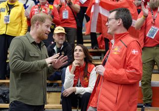 Prince Harry wears a khaki green shirt and talks to Prince Joachim and Princess Marie of Denmark at Sitting Volleyball as part of the Invictus Games 2025 in Canada