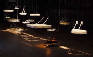 Exhibition hall with grand pianos and large metal lighting structures hanging from the ceiling