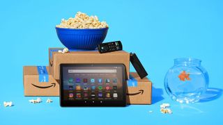 An Amazon fire tablet leaning against amazon boxes with an amazon fire stick remote and popcorn on top