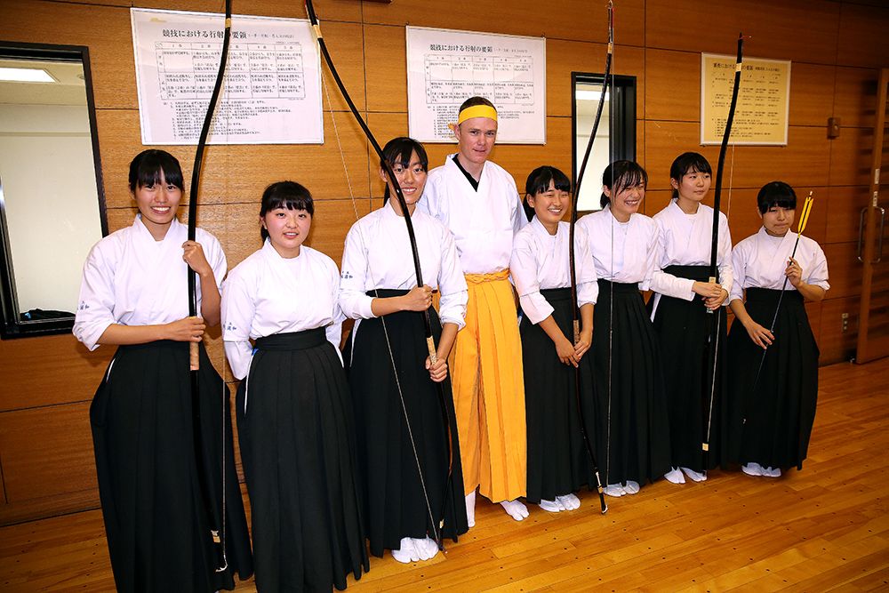 Chris Froome in his archery gear lines up alongside local pupils
